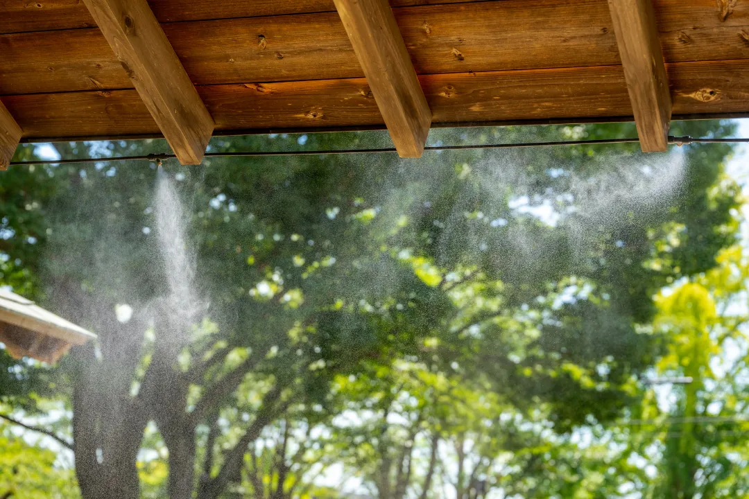 Mosquito misting system spraying a fine mist from a covered patio into a tree-lined backyard
